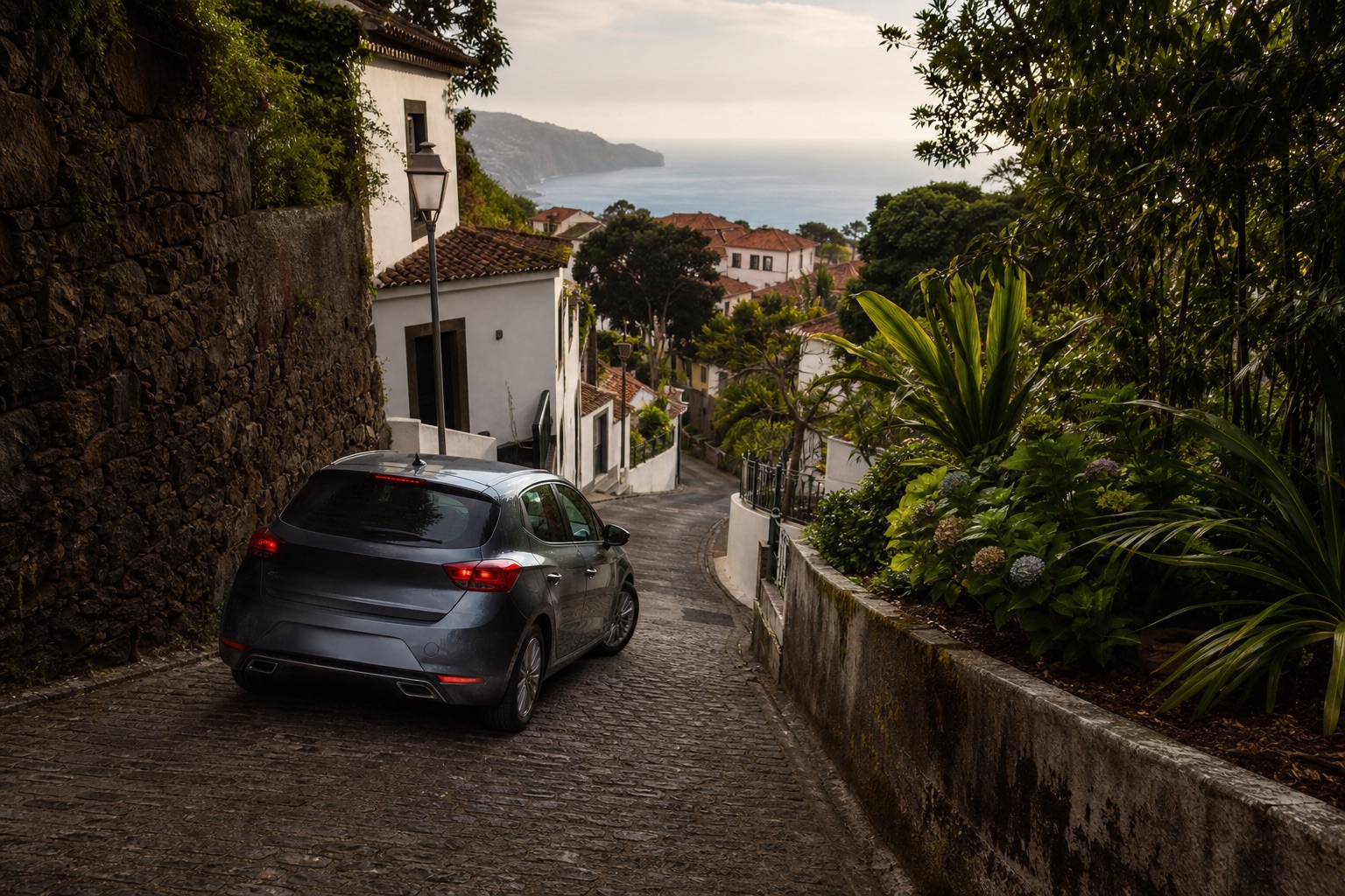 A compact car descending a steep, narrow Madeira street framed by volcanic stone and subtropical plants